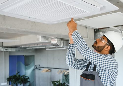 Indian male worker inspecting the air conditioner mounted on the ceiling.