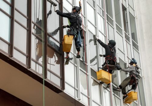 Industrial mountaineering workers hangs over residential facade building while washing exterior facade glazing. Rope access laborers hangs on wall of house. Concept of industry urban works. Copy space